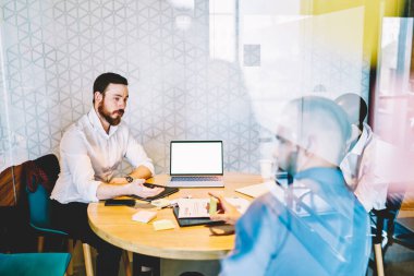 Resmi gömlekler giymiş, dizüstü bilgisayarlı masada oturan modern ciddi iş arkadaşları ofis alanındaki akıllı telefonu belgelerler. 