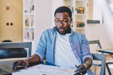 Neşeli Afro-Amerikalı adam modern ofisteki masanın planlarını incelerken heyecandan homurdanıyordu.