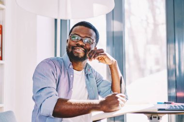 Siyah gülümseyen entellektüel düşünceli yazar, güneşli odada kalem ve defterle otururken kompozisyon yazıyor. 