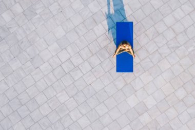 Nilüfer çiçekli mavi yoga minderinin üzerinde rahatça oturan ve gün ışığında taştan zeminde dinlenen sağlıklı insan görüntüsü.