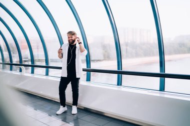 Beyaz tişörtlü karizmatik gülen adam kollarını sıvadı ve beyaz spor ayakkabılar, yaya köprüsünde kulaklıkları ayarlayan müzik dinlemek için cep telefonu kullanıyor.