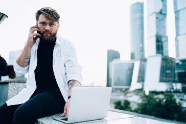 Önemli uluslararası akıllı telefon konuşmaları, dolaşım iletişimi ve uzaktan çalışma kavramları yaparken kameraya bakan, optik gözlüklü, ciddi bir erkek programcının portresi