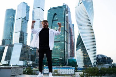 Metropolis 'i gezmeyi kutlayan şehir merkezinde kameraya gülümseyen, gökdelenlerin arkasında poz veren mutlu bir adamın uzun boylu bir portresi.