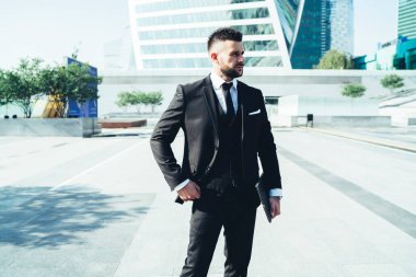 Siyah takım elbiseli yakışıklı bir erkek, parlak güneşin altında modern şehrin caddesinde duran meslektaşıyla buluşmayı bekliyor.