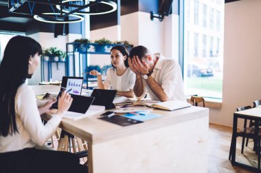 Odaklanmış kadın ve yorgun adam yeni başlatılan projeleri tartışırken aynı anda açık modern ofiste oturuyor ve birlikte çalışıyorlar.