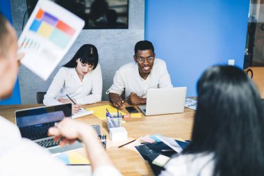 Modern erkek ve kadın işçiler istatistik kağıtları ve cihazlarla masada toplanıp şirkette iş planlarını tartışıyorlar. 