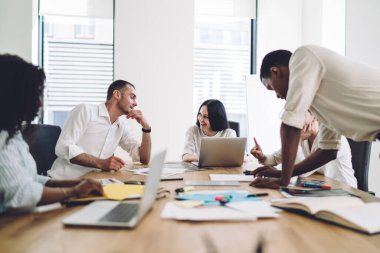 İş toplantılarında belgelerle uğraşan çok ırklı bir ekip neşeli ve pozitif meslektaşlar konuşurken ve eğlenirken.