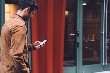 New York caddesindeki cam girişe doğru yürüyen ve akıllı telefondan yazan şık giyinmiş gülümseyen genç bir erkek.