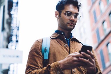 Alttan bakınca, kulaklıklı, kahverengi süet ceketli, akıllı telefondan yazan ve New York caddesinde dururken müzik dinleyen düşünceli, yakışıklı, tıraşsız bir erkek görüyorum.