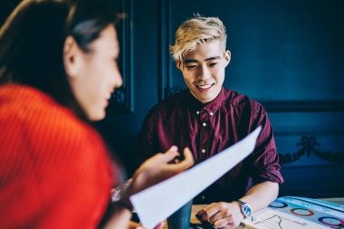 Gündelik giysiler içinde gülümseyen çok ırklı iş arkadaşları ellerinde kağıtlarla bürodaki diyagramlarla masada oturuyorlar. 