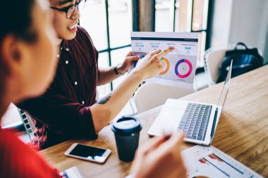 Gelişigüzel giyinmiş, modern iş yerinde proje grafiklerini kontrol eden dizüstü bilgisayarları tartışan zeki genç iş arkadaşlarının tepesinden. 