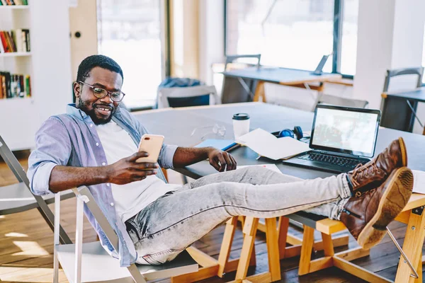 Cheerful Optimistic African American Male Glasses Sitting Chair Legs Table — Stock Photo, Image