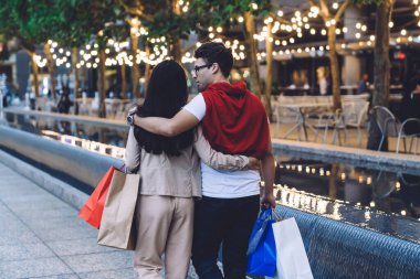 Günümüz modern çifti şefkat ve konuşmayla kucaklaşıp alışveriş torbalarıyla şehir caddesinde yürürken.