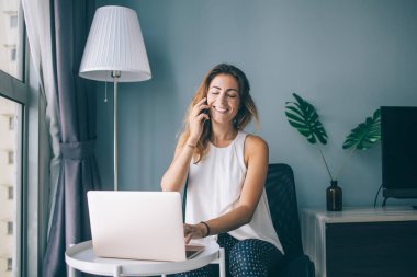 Beyaz kadın evde dinleniyor. En iyi arkadaşıyla yaptığı akıllı telefon konuşmasında seviniyor. Mutlu gülümseyen hippi kız dizüstü bilgisayarda oturuyor ve cep telefonuyla konuşuyor.