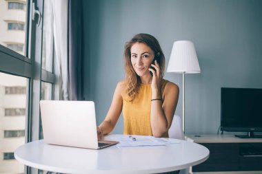 Modern dizüstü bilgisayar ve bütçe muhasebe raporuyla evde oturan pozitif kadın serbest yazar portresi, cep telefonu cihazıyla arama yapan başarılı kadın Netbook sistemini tartışıyor.