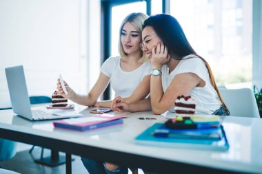 Gündüz vakti iyi aydınlatılmış çalışma odasında ödev hazırlarken çıkartma notundan bilgi okuyan gündelik genç kız arkadaşlar.