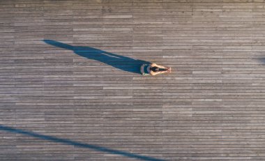 Tanınamayacak haldeki atletik ve zayıf kadının tahta zeminde kollarını açması ve yoga pratiği sırasında esneklik göstermesi.
