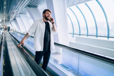 Siyah tişörtlü ve beyaz tişörtlü hoş sakallı adam cep telefonuyla konuşuyor hafif geometrik tünelde tırabzan tutuyor.