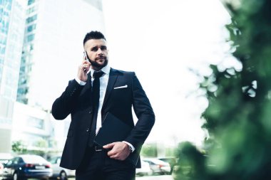 Siyah takım elbiseli yakışıklı genç adam iş yerinde iş arkadaşı serbest çalışma projesiyle konuşmak için cep telefonunu kullanıyor.