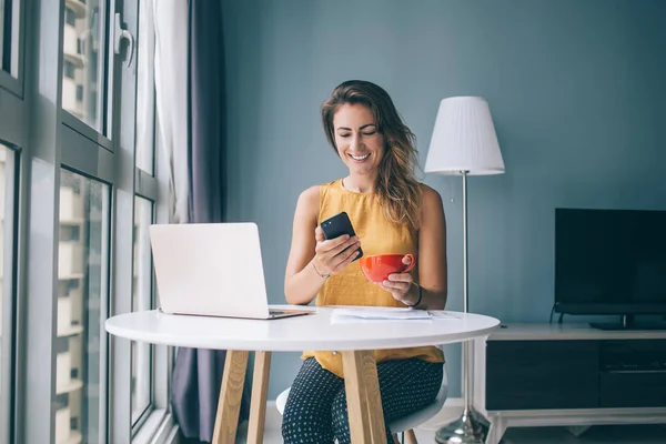 Молодая Улыбающаяся Женщина Сидящая Круглым Столом Ноутбуком Чашкой Чая Просматривающая — стоковое фото