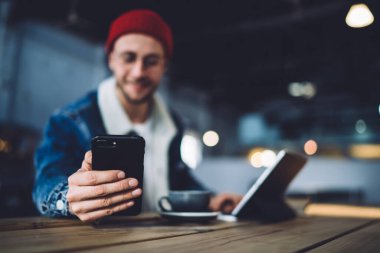 Çatı katında tablet ve bir bardak içkiyle masada otururken mesajlaşmak ve iletişim kurmak için modern dijital aletle internette sörf yapan mutlu adam.