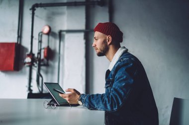 Genç dalgın sakallı, stil sahibi serbest stil sahibi, sıcak mavi kot ceket giyen, kırmızı şapkalı iş yerindeki aletleri kullanan
