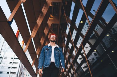 Tablet taşıyan ve şehir merkezinde modern cam gökdelenlerle gezen modaya uygun giyinmiş neşeli bir adamdan.