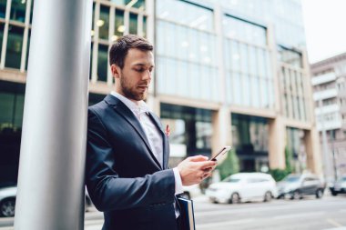 Şehir merkezinde ışık direğine yaslanırken resmi kıyafetlerle başarılı bir yetişkin erkek müdür cep telefonundan mesaj atıyor.