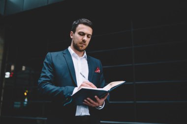 Modern şehir caddesinde dikilirken randevu defterine not alan resmi şık takım elbiseli yakışıklı erkek yöneticilerden. 