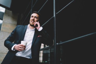 Şık giyinmiş, şık bir genç adam akıllı telefon kullanıyor işten dinlenen bir arkadaşı dinliyor şehir sokağında taze içecek içiyor ve başka yöne bakıyor.