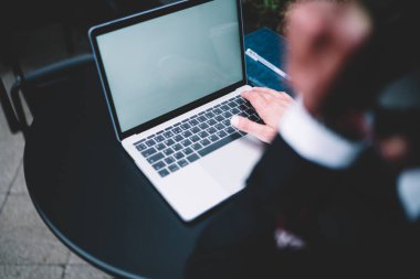 Masada defter ve kalemle yazı yazan koyu renk takım elbise uzmanının modern dizüstü bilgisayarından.