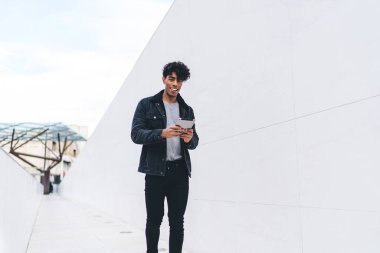 Modern stil gülümseyen pozitif esmer Afrikalı Afrikalı Amerikalı adam gün ışığında şehir caddesi tünelinde yürürken tablet üzerinde geziniyor.