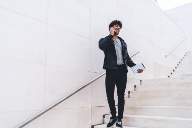 Modern stil güler yüzlü genç esmer Afrikalı Amerikalı adam telefonda konuşurken gündüz vakti şehir merdivenlerinde yürüyordu.