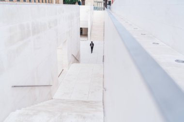 Beyaz fayanslı sokak merdivenleri perspektifli ve ceketli sıradan modern bir adam gündüz vakti uzaklarda yürüyor.