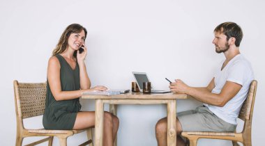 Gayri resmi giyinmiş, sakallı, yetişkin bir erkeğin cep telefonuyla dolaşırken beyaz arka plandaki akıllı telefondan konuşan neşeli, güzel bir kadının yan görüntüsü.