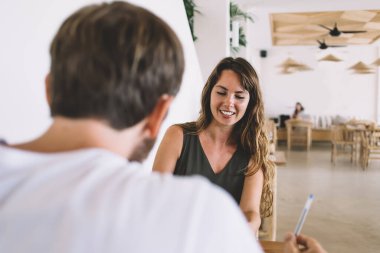 Keyifli, genç ve güzel bir bayanın günlük kıyafetleriyle kafeteryada elinde kalemle oturması. 