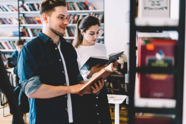 Gündelik giysiler içinde neşeli rüyalar gören genç bir öğrenci kütüphanede üniversite projesi kitabı okumak için sınav için bilgi arıyor.
