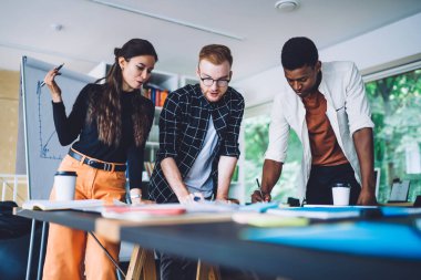 Çağdaş çalışma ortamında yaratıcı proje üzerinde çalışırken çok ırklı gençler taslak çiziyor ve birbirleriyle konuşuyorlar.