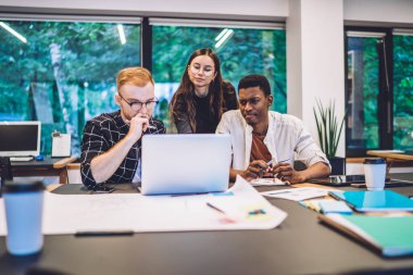 Kütüphanedeki ders projesinde çalışırken dizüstü bilgisayara bakarak sorunu çözmeye odaklanmış çok ırklı öğrenciler.
