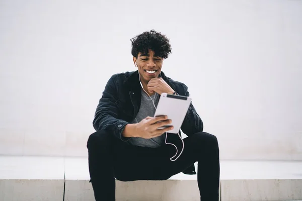 Afroamerykanin Uśmiechnięty Młody Mężczyzna Dotykający Podbródka Siedzący Białych Schodach Podczas — Zdjęcie stockowe