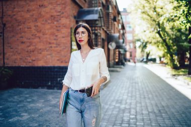 Ellerinde modern cep telefonu aygıtı ve ekipmanlarıyla gezen göz koruması sağlamak için optik gözlük takan yüz yıllık bayan öğrenci, İspanyol nesil Z