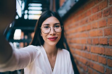 Yüzünde sevimli bir gülümseme olan çekici bir hippi kızın, şehir merkezinde boş zamanlarında selfie çekerken, güzel bir kadının açık havada kendi fotoğrafını çekerken yakın plan portresi.