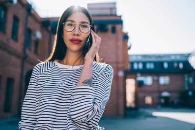 Gözlüklü çekici bir kızın yarı boy portresi. Şehir sokağındaki boş zamanlarında kameraya bakıyor. 4 g 'lik interneti telefonla kullanan güzel bir kadın.