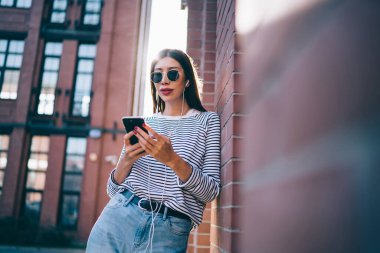 Millennial hipster kızı güneş gözlüklü açık havada duruyor ve sosyal ağların paylaşımı için popüler müzik setini, sesli kitabı ve mesajları dinleyen genç bir kadını konu alan metin eleştiri yayınları yazıyor.