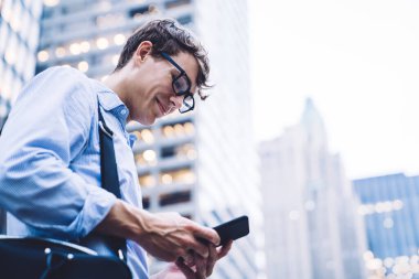 New York 'un arka planında duran, çantalı, çantalı, cep telefonlu, tişörtlü ve gözlüklü işçilerin yan görüntüsü.