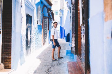 Fas 'ın ünlü şehri Chefchaouen' de mavi caddelerde dikilirken günlük kıyafetleriyle kameraya bakan düşünceli genç turistin yan görüntüsü.