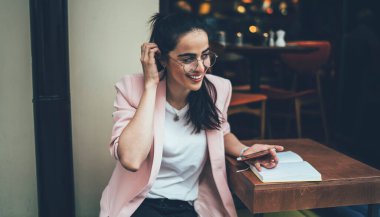 Gündelik giysiler ve gözlüklerle gülümseyen çekici bir etnik kadın. Arkadaşlarıyla cep telefonu mesajlaşmaları, not defterindeki notları okuması, kafedeki saçları düzeltmesi.
