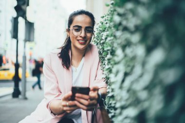 Modern şehrin kentsel sokaklarında kameralara bakarak arkadaşlarıyla akıllı telefon mesajları kullanan gündelik kıyafetleri ve gözlükleriyle hoş bir bayan.