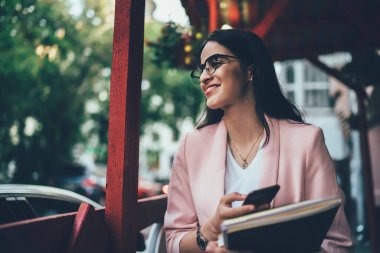 Havalı giyinmiş, gözlüklü, sosyal medyada sörf yapan, kafede vakit geçiren heyecanlı etnik gülümseyen kadın.