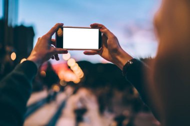 Boş dokunmatik ekranlı modern cep telefonuna seçici odaklanma. Fotoğraf çekmek için kamera kullanılıyor. Milenyum kadını, reklam sitesi için cep telefonuyla fotoğraf çekiyor.